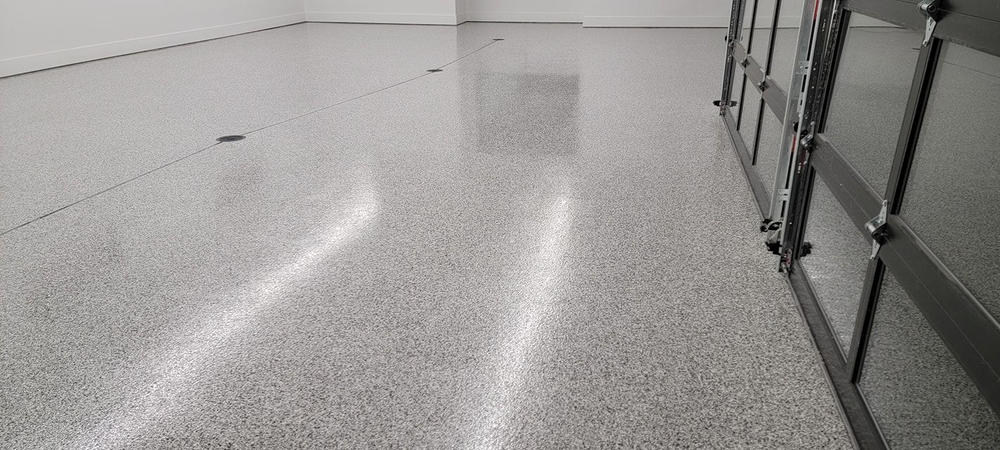 Gray speckled epoxy floor reflecting light, adjacent to a metal gate in a room.