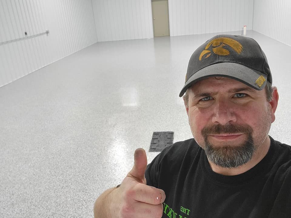 Man in cap gives thumbs up in a white-walled, epoxy-floored room.