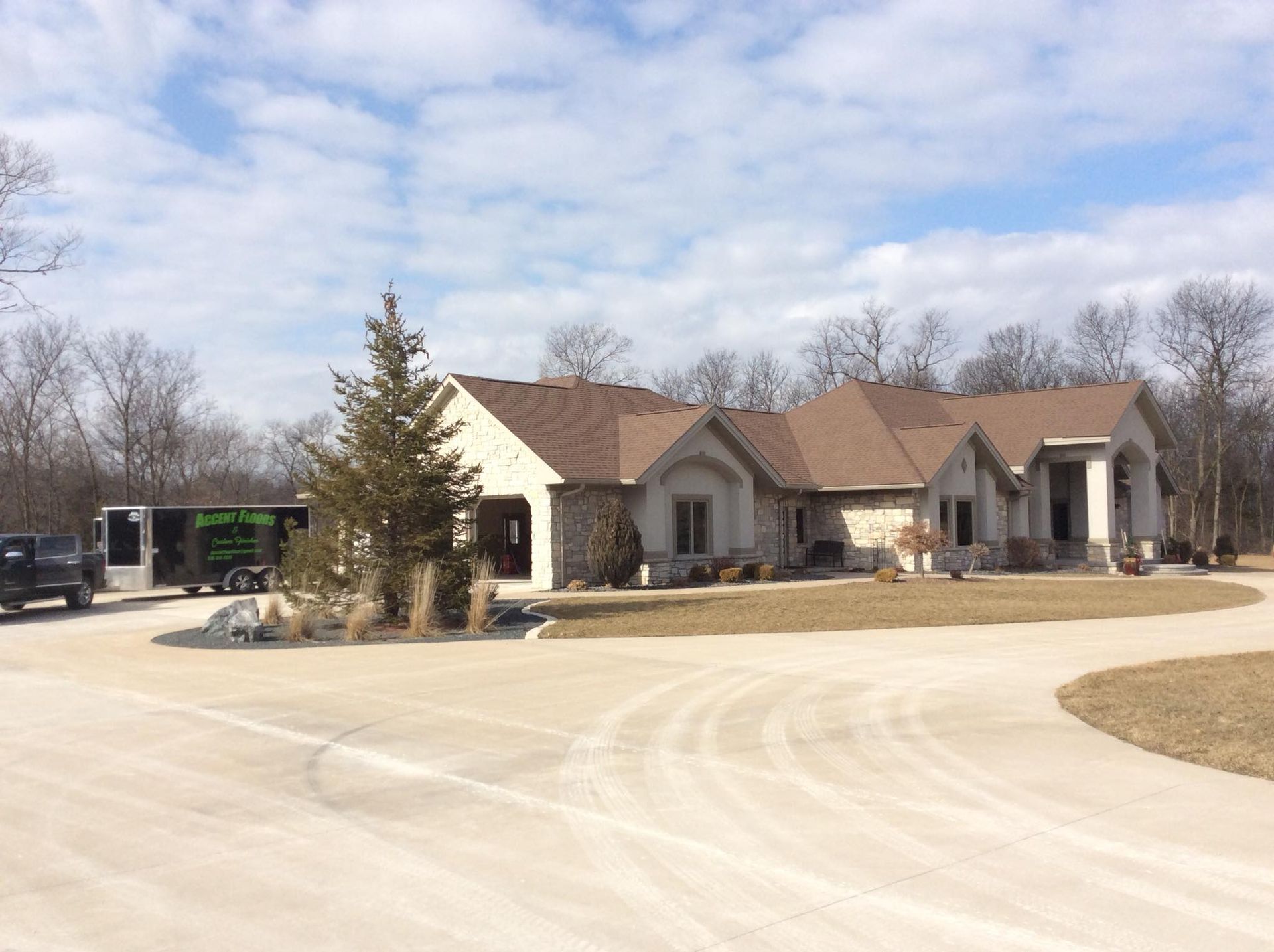 A large, light-colored house with a circular driveway. A moving truck is parked in front.