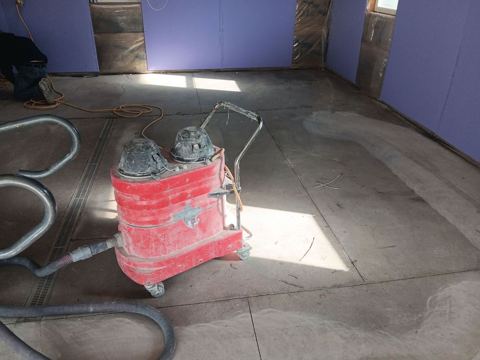 Red floor sander on a concrete floor, inside a room with drywall, dust visible.