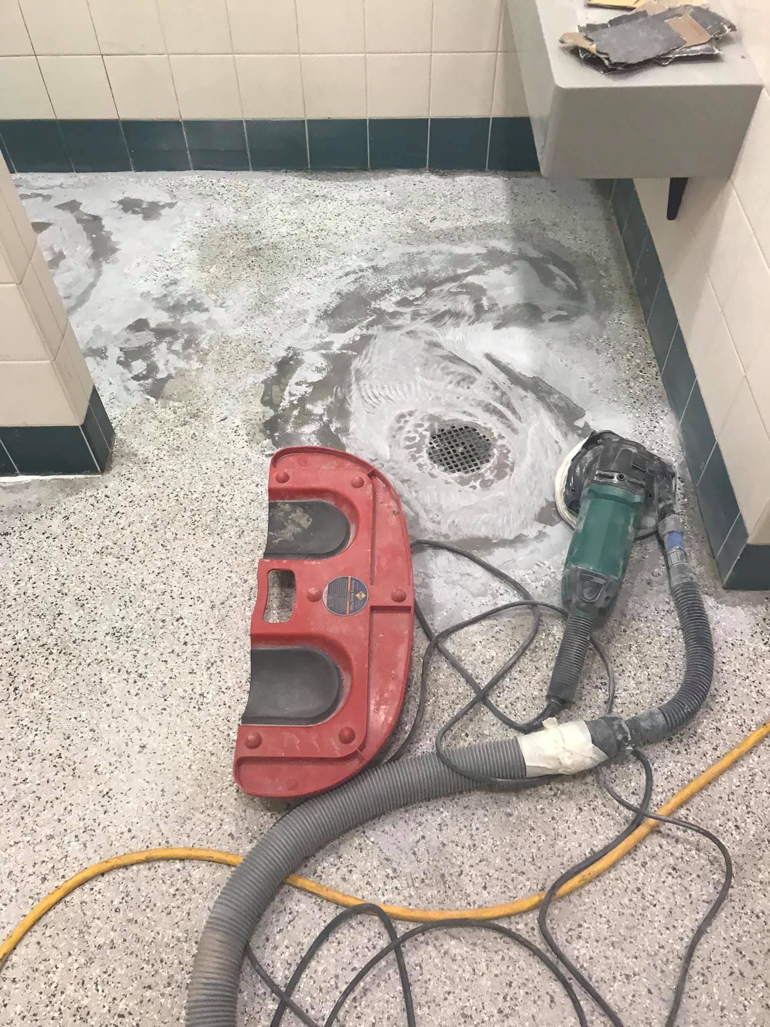 Floor grinding in a bathroom; a worker is using a tool to remove old sealant, revealing the speckled tile.