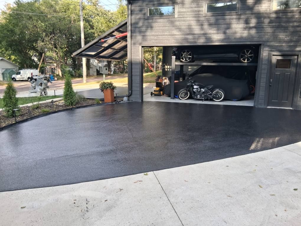 Blacktop driveway leads to a modern garage holding a car and motorcycle.