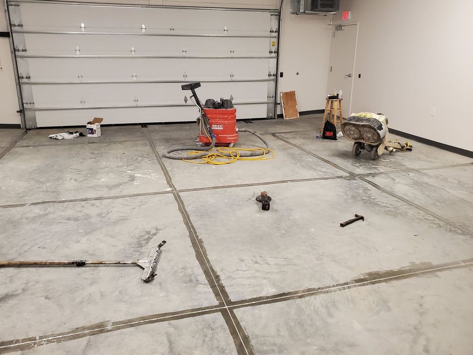 Garage interior with concrete floor, tools, and equipment scattered throughout. Garage door is open.