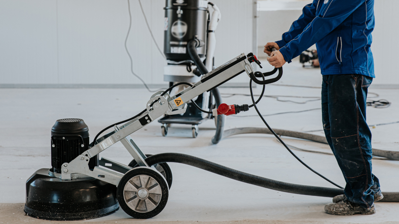 Person operating a floor grinder on a concrete floor, industrial setting.