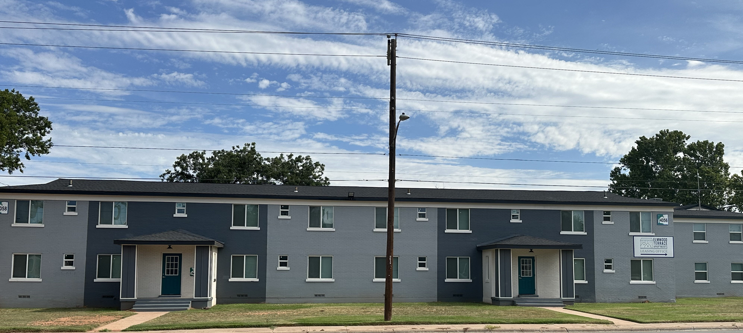 Two-story apartment building with gray and dark blue facade under a blue sky with clouds.