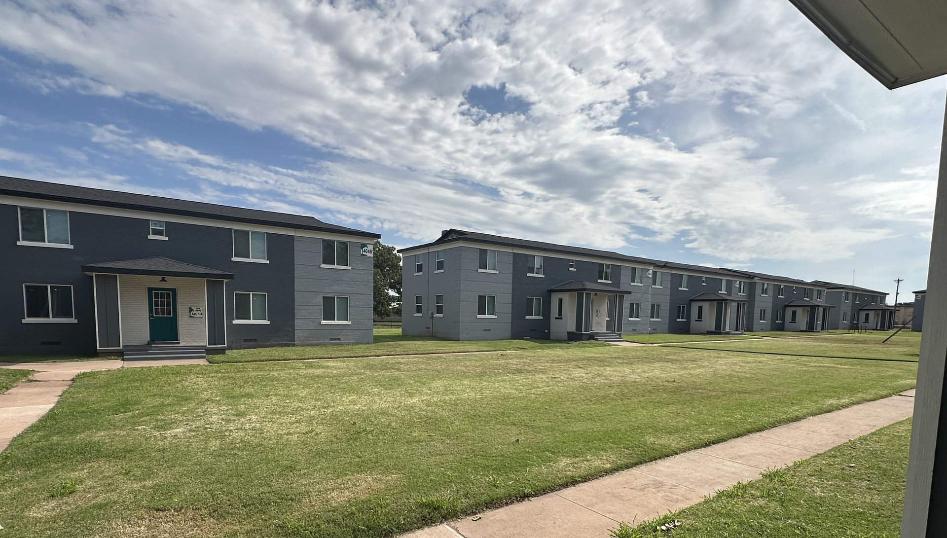 Rows of blue two-story apartment buildings with white trim, set on a grassy field under a cloudy sky.