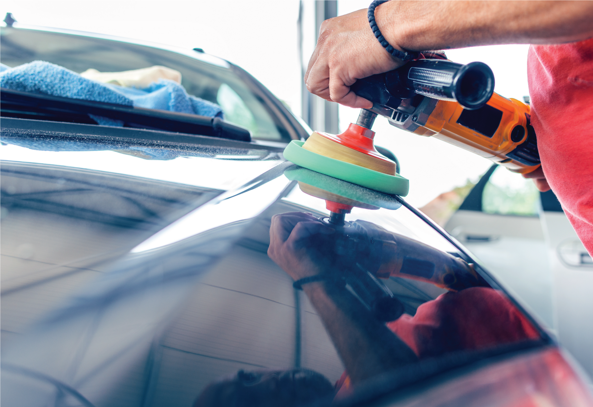 A man is polishing the hood of a blue car with a machine.