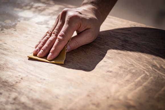 main qui sable meuble en bois