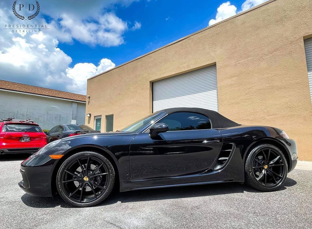 Black Porsche convertible parked in front of a tan building, on a sunny day.