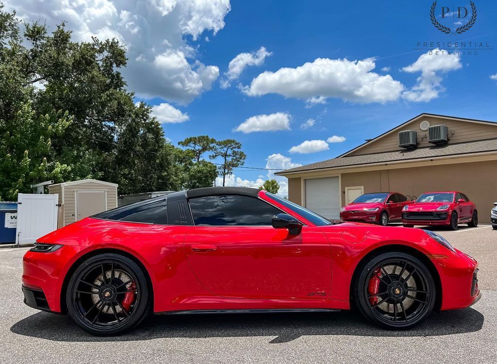 Red Porsche Targa parked outside under a blue sky. Black wheels, roof, and tinted windows.