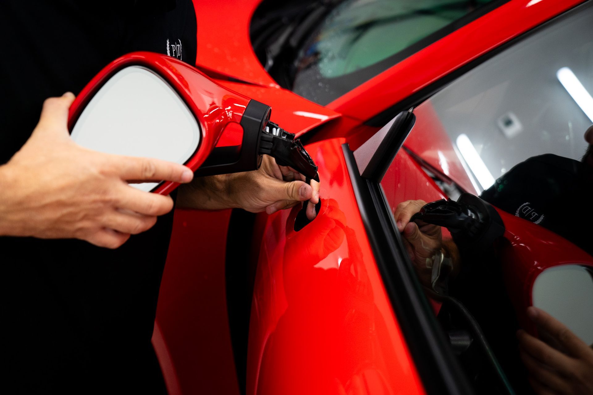 Person installing a red side mirror on a red car.