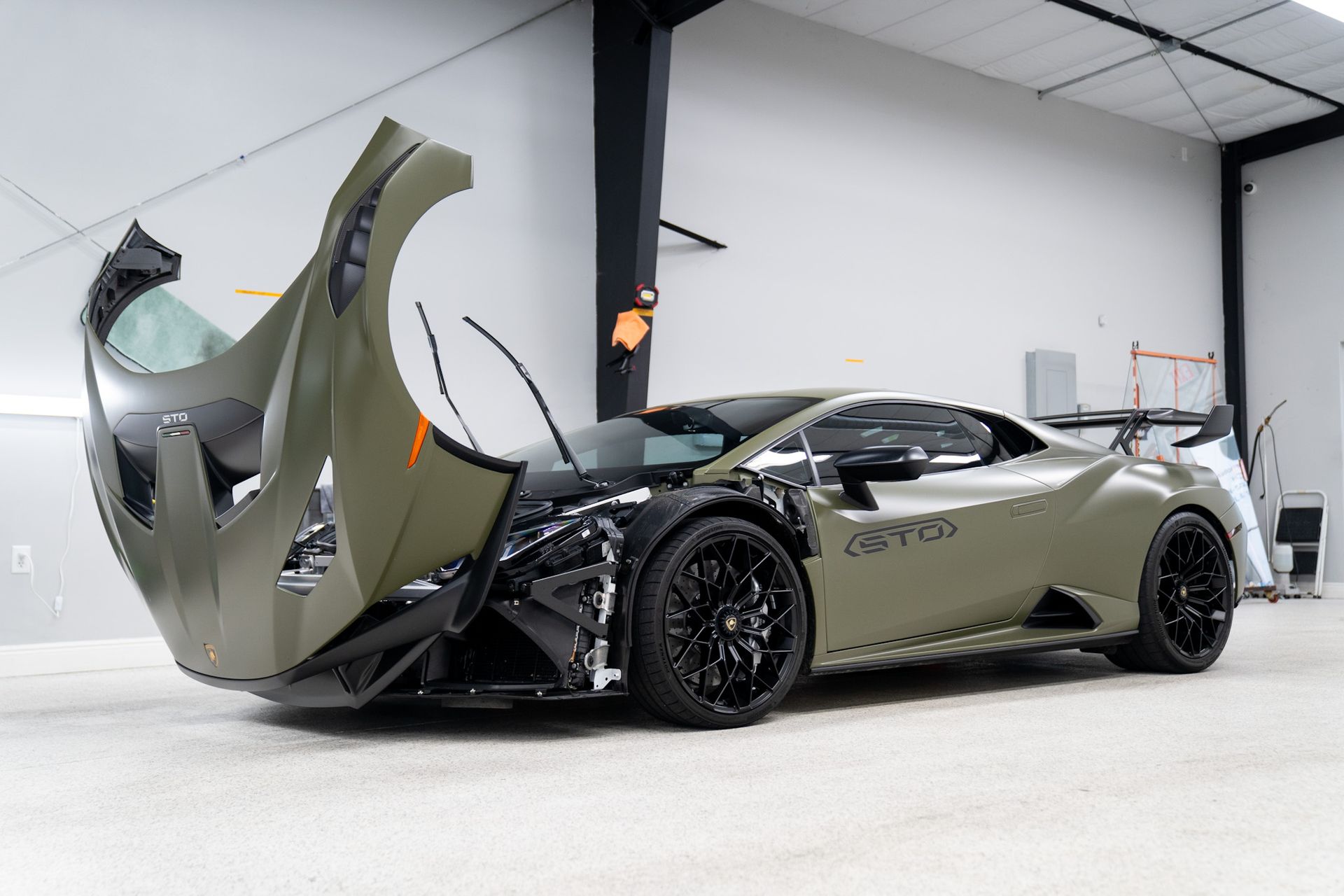 Olive green Lamborghini with raised hood and missing front panel, in a garage.