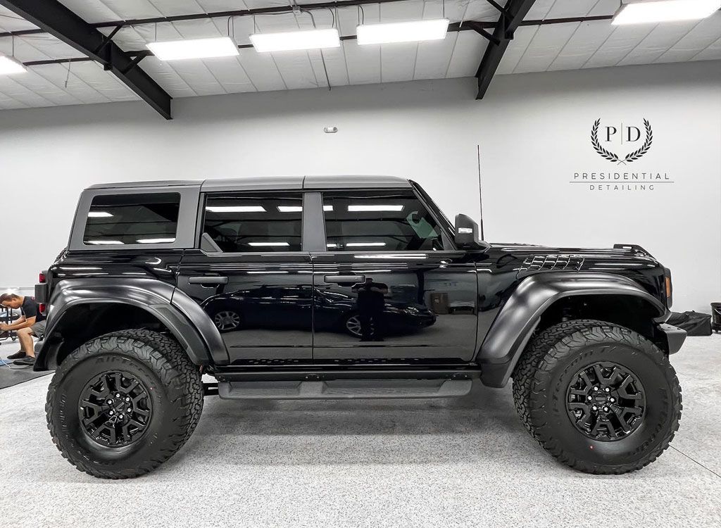 Black Ford Bronco SUV parked indoors, black wheels and fender flares, logo in background.