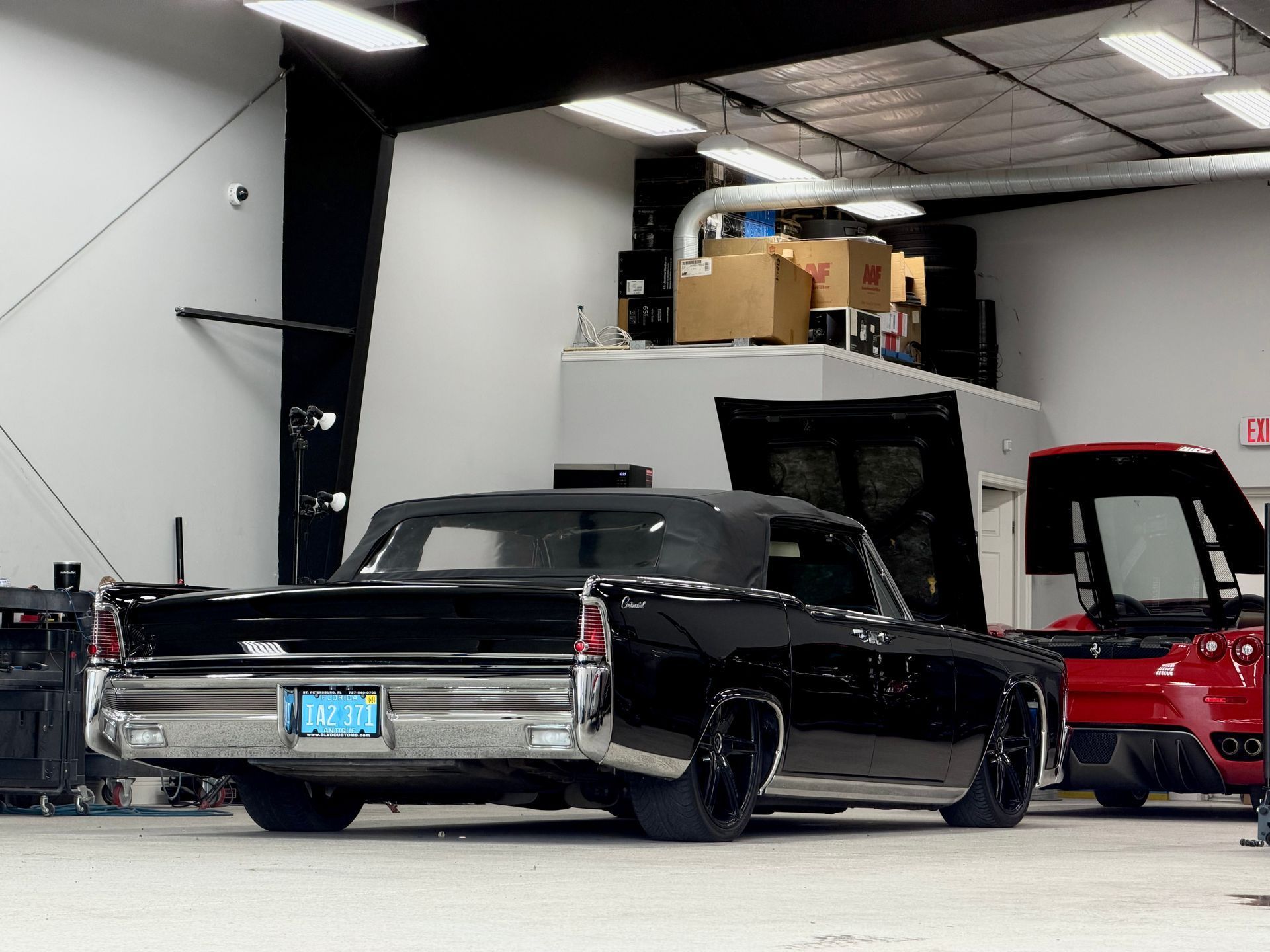 Black convertible classic car in a garage with a red car visible to the right.