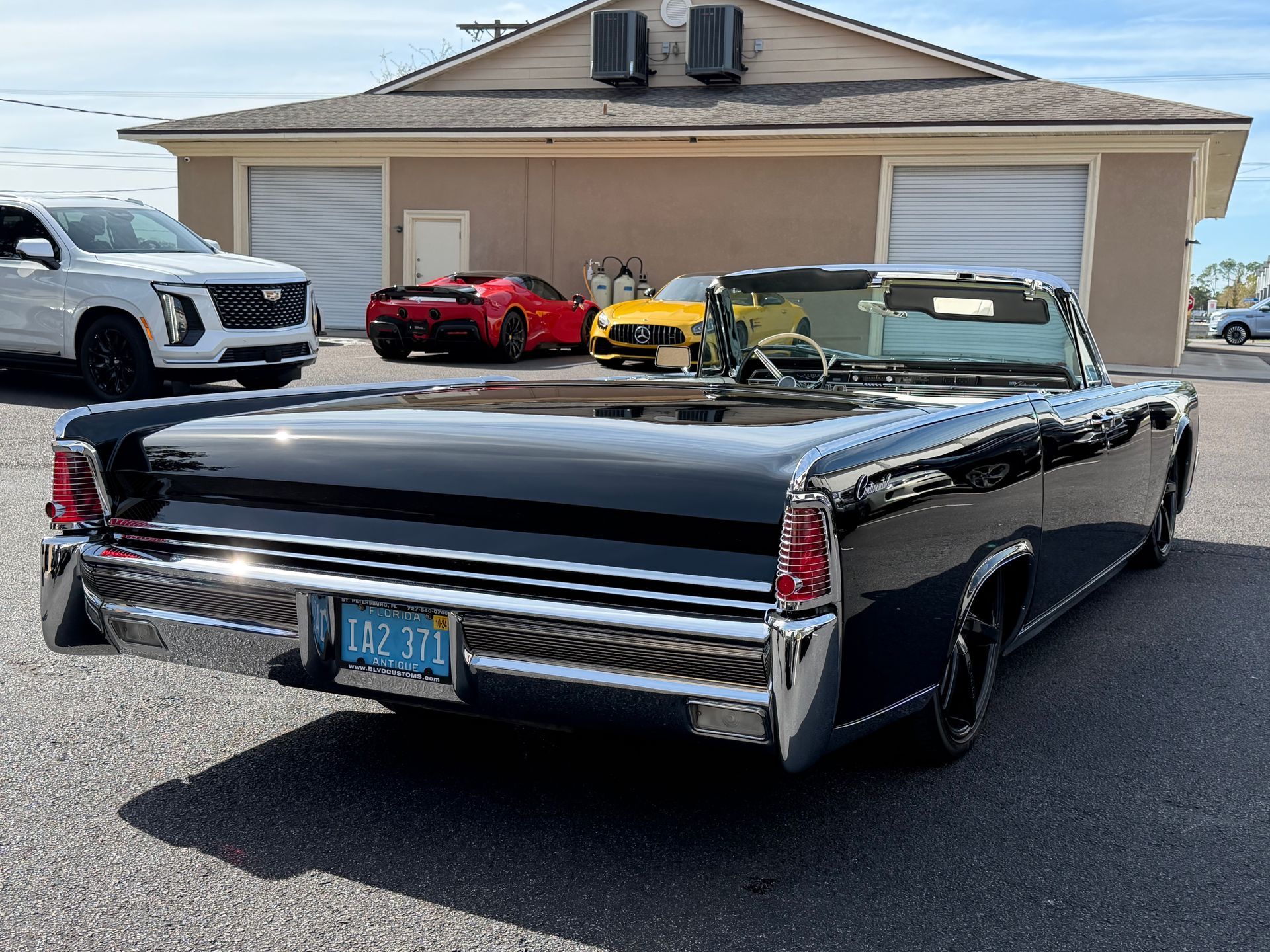 Black convertible car parked outside a building. Other cars in background, clear sky.