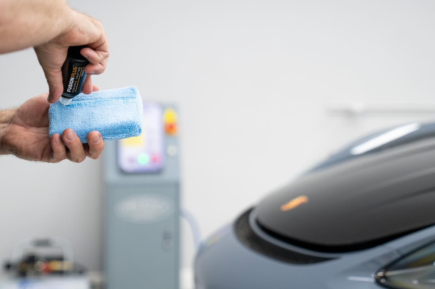 A person is holding a microfiber cloth in front of a car.