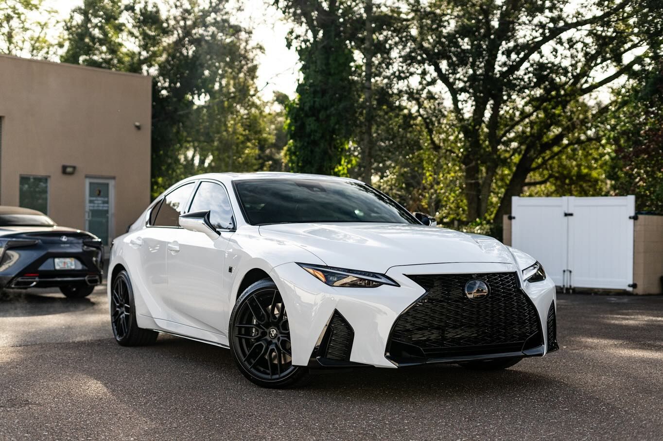 White Lexus sedan with black wheels parked outside near a building and trees.