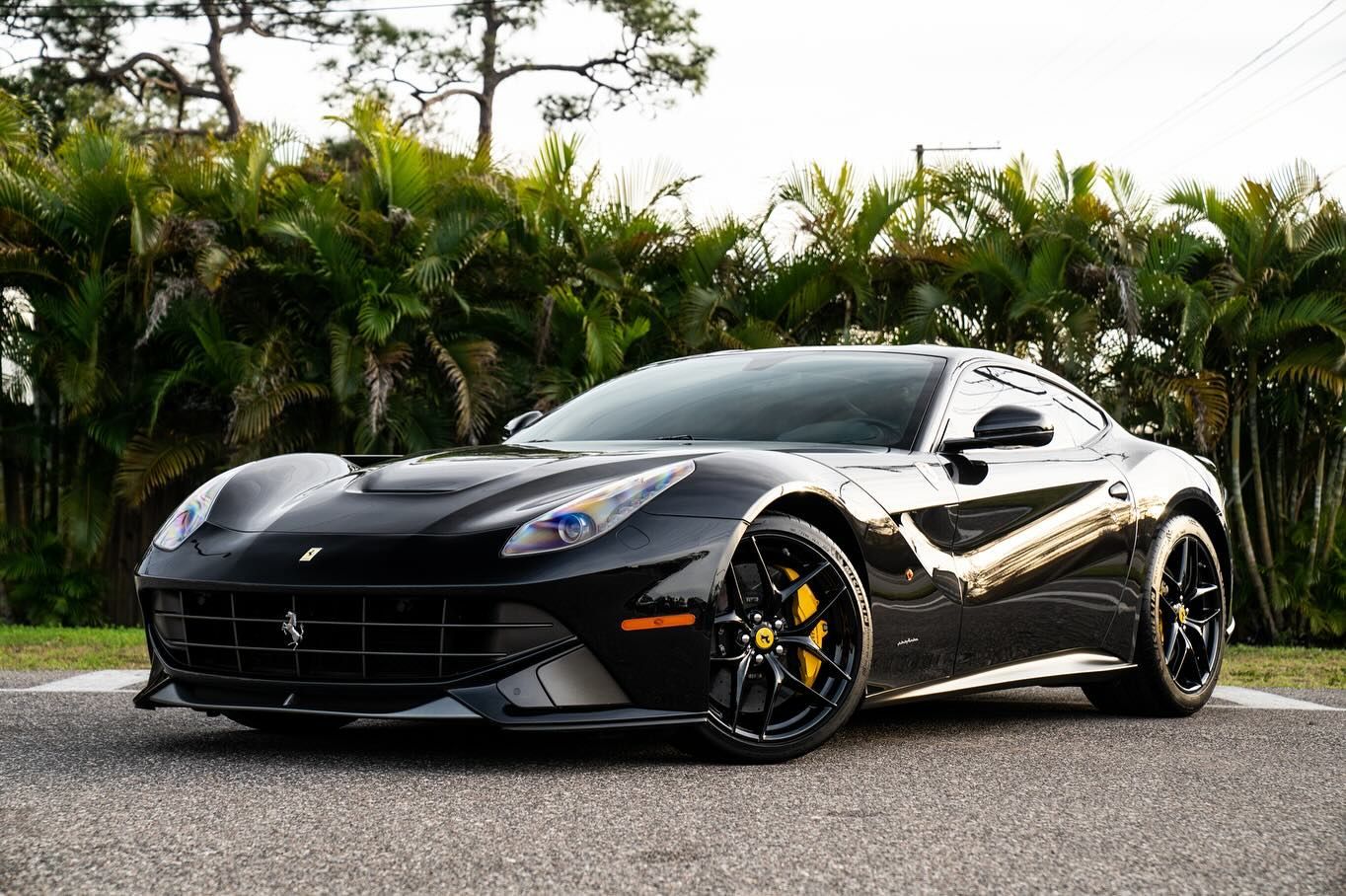 Black Ferrari sports car parked on pavement, yellow brake calipers visible.