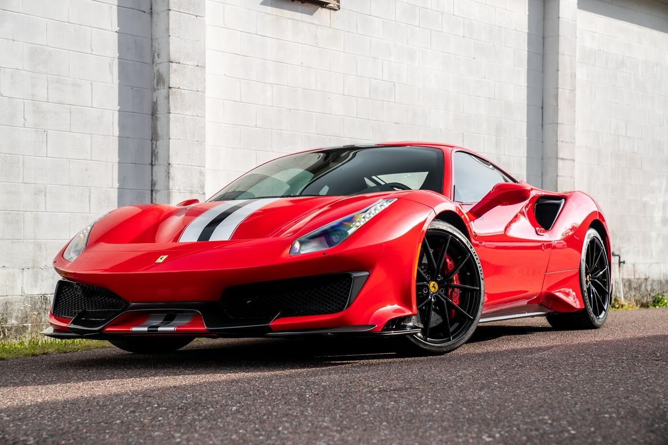 Red Ferrari sports car with white racing stripes parked in front of a white wall.