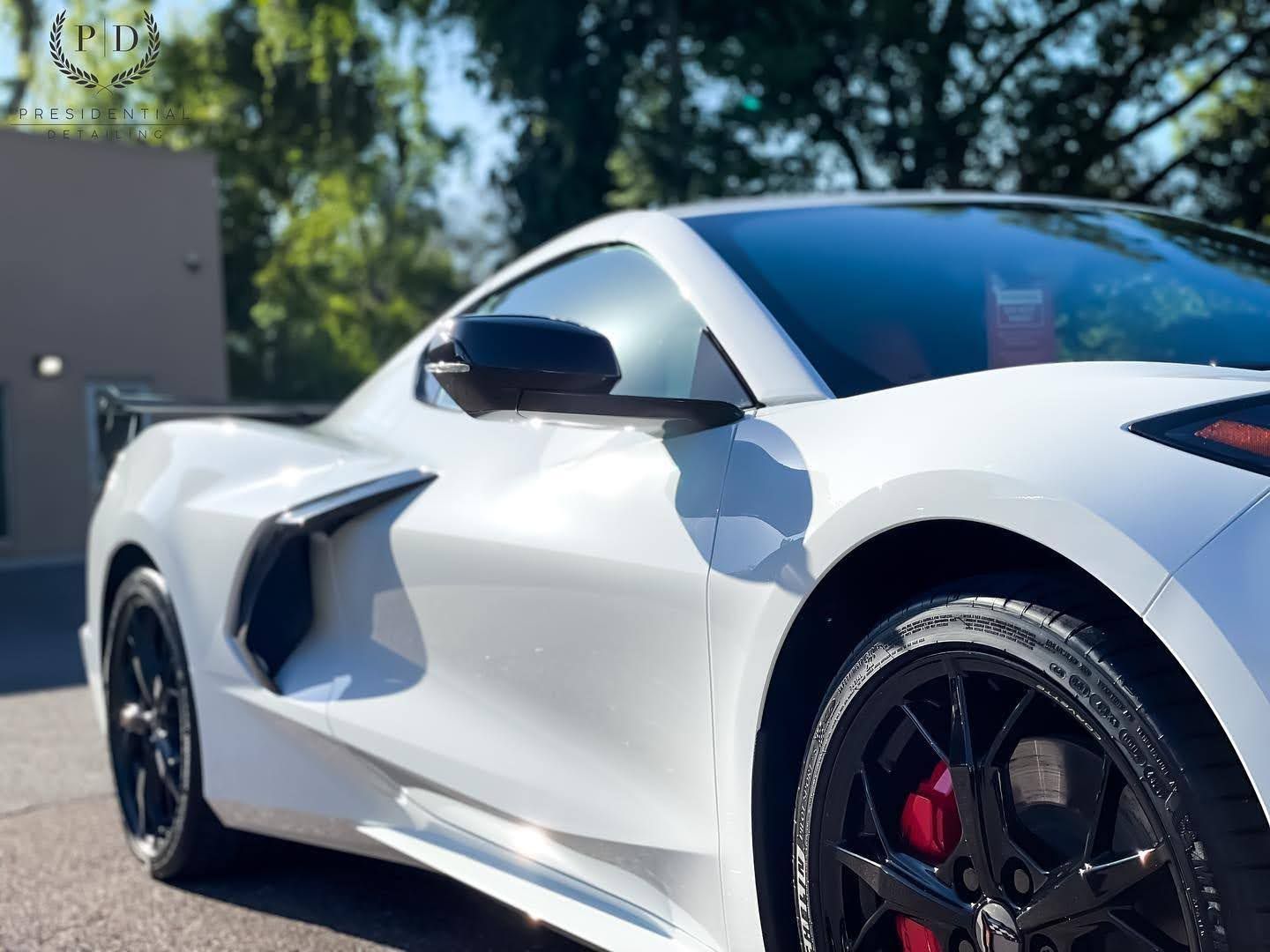 White sports car parked outdoors with black wheels and red brake calipers in sunlight