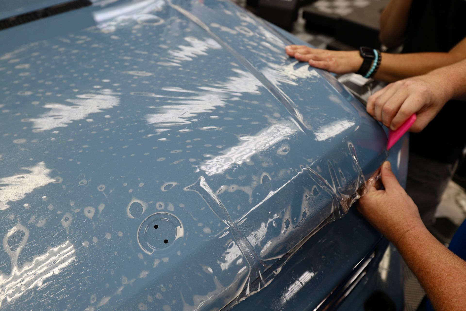 A person is covering the hood of a car with plastic wrap.