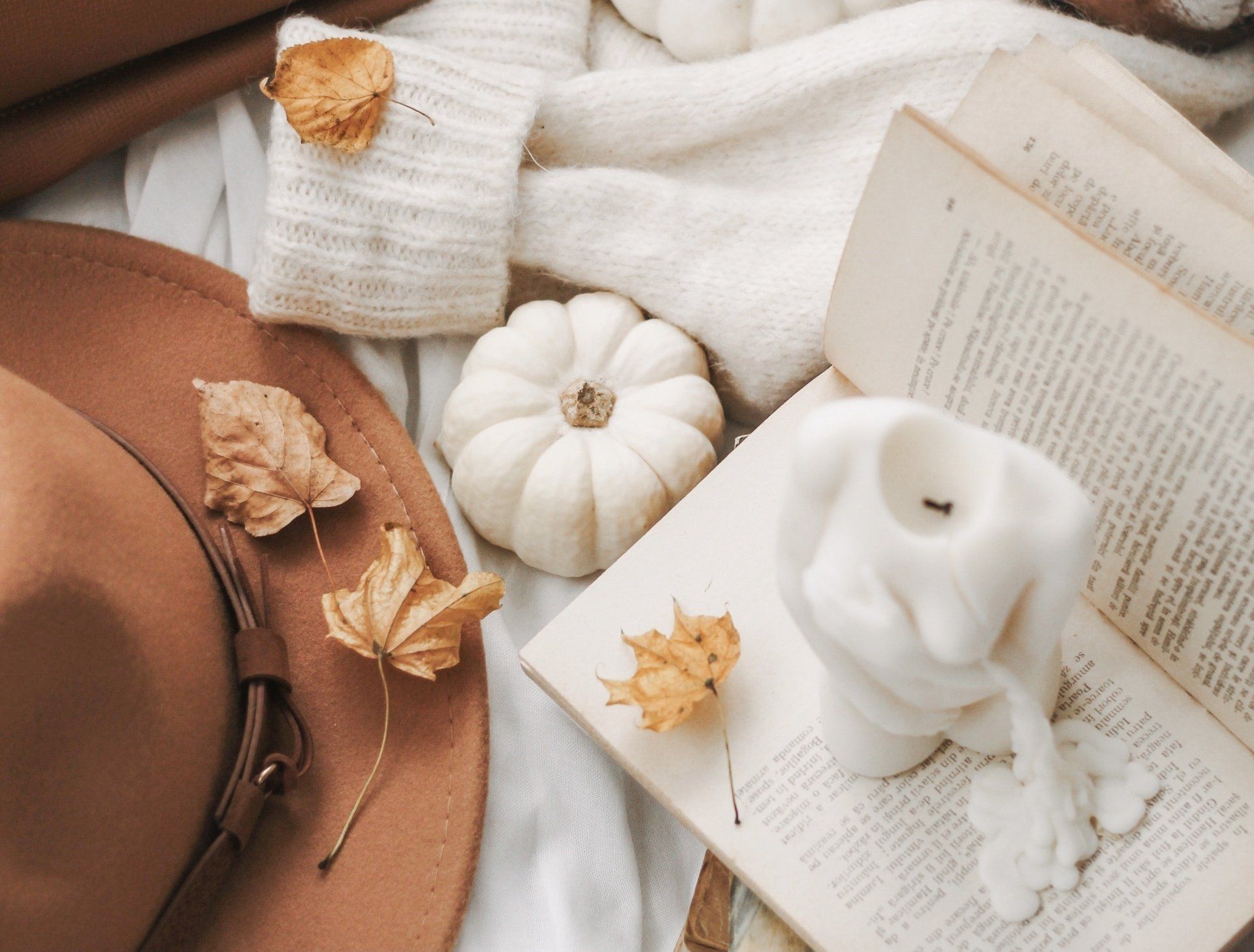 Fall flat lay with brown hat, leaves, white pumpkins, a white sweater, and a white candle