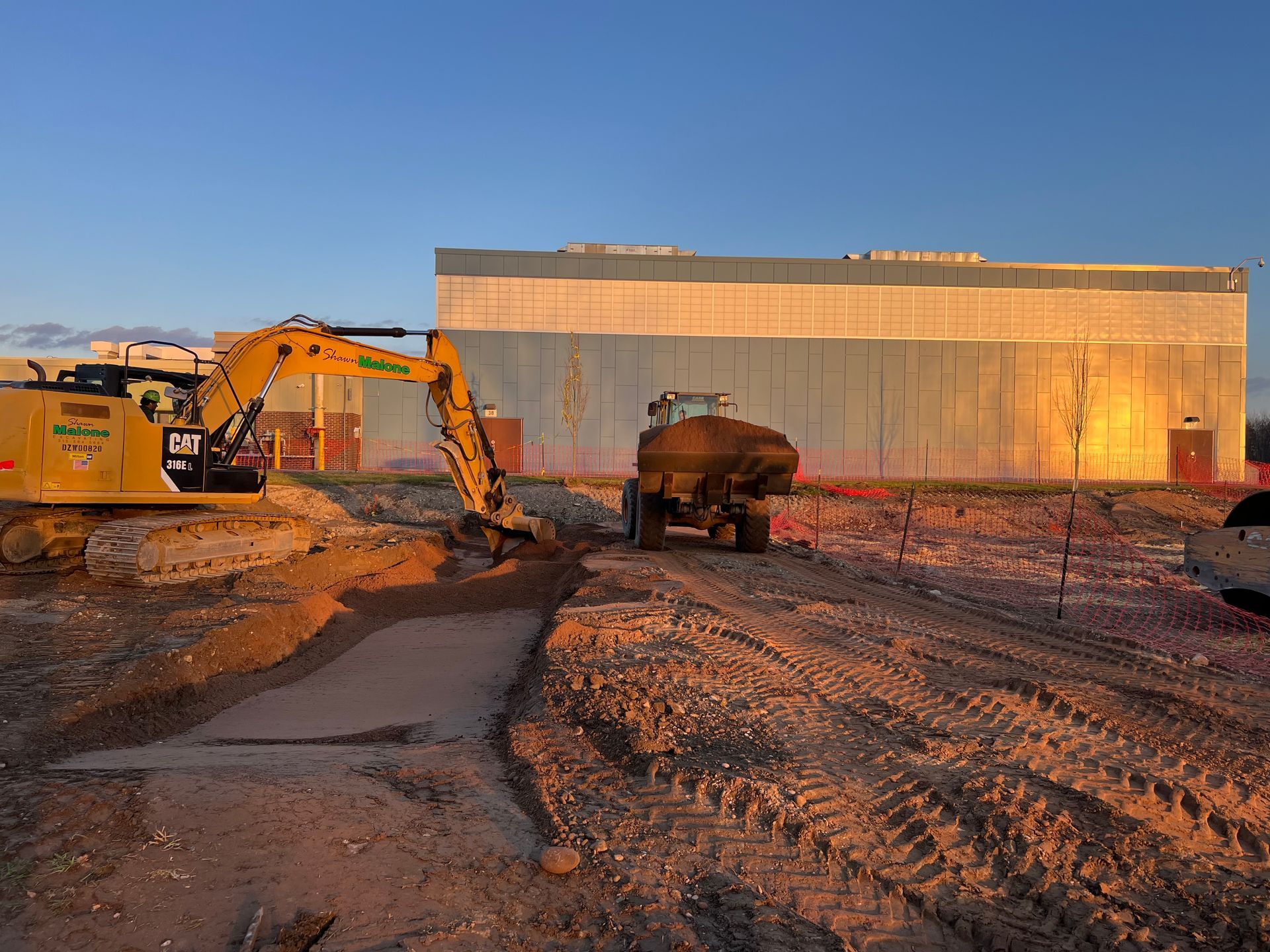 Green dump truck unloading dirt onto a grassy area with a red barn in the background.