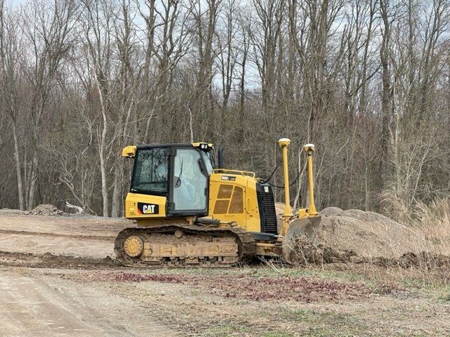 Yellow Caterpillar bulldozer plowing dirt, near trees.