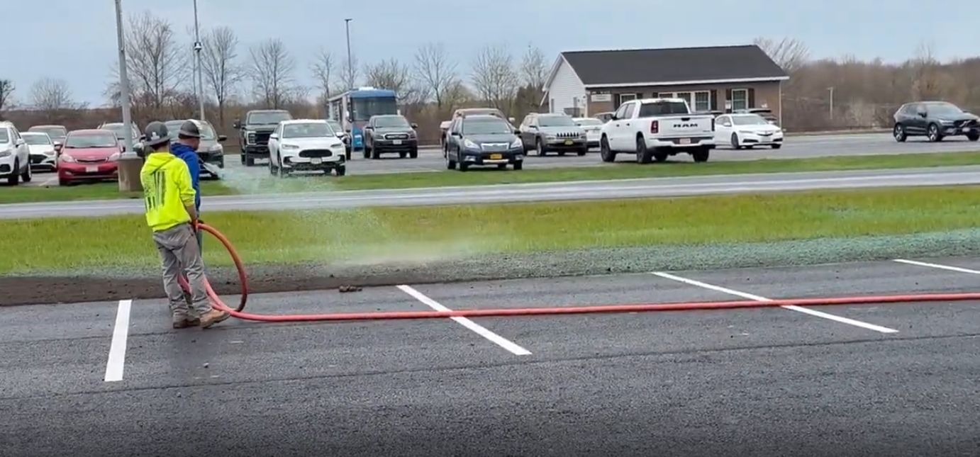 Yellow CAT excavator on a rocky shoreline, working. Cloudy sky, water visible.