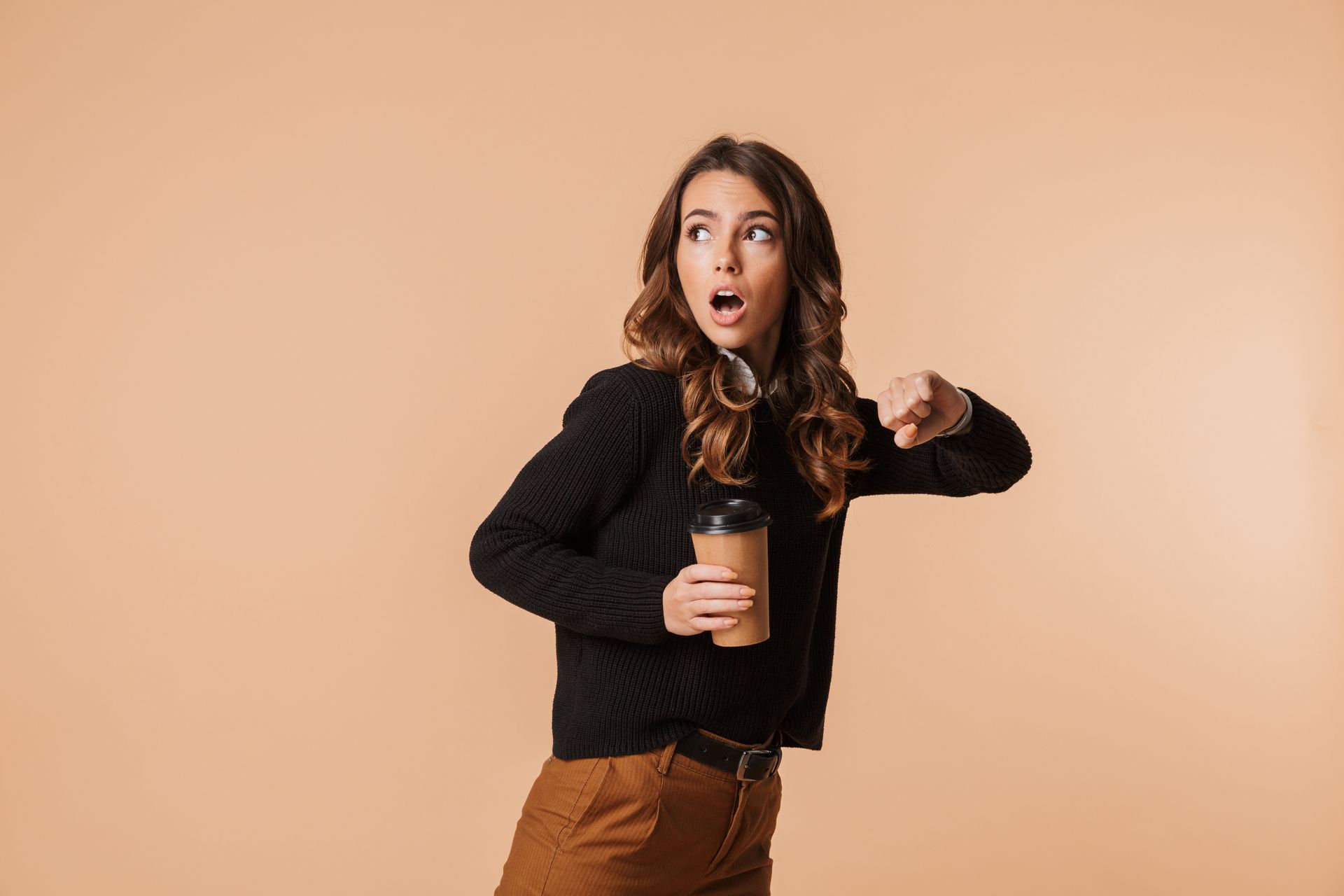 A person in a black sweater holds a coffee cup, looking surprised and checking their wrist watch. Neutral background.