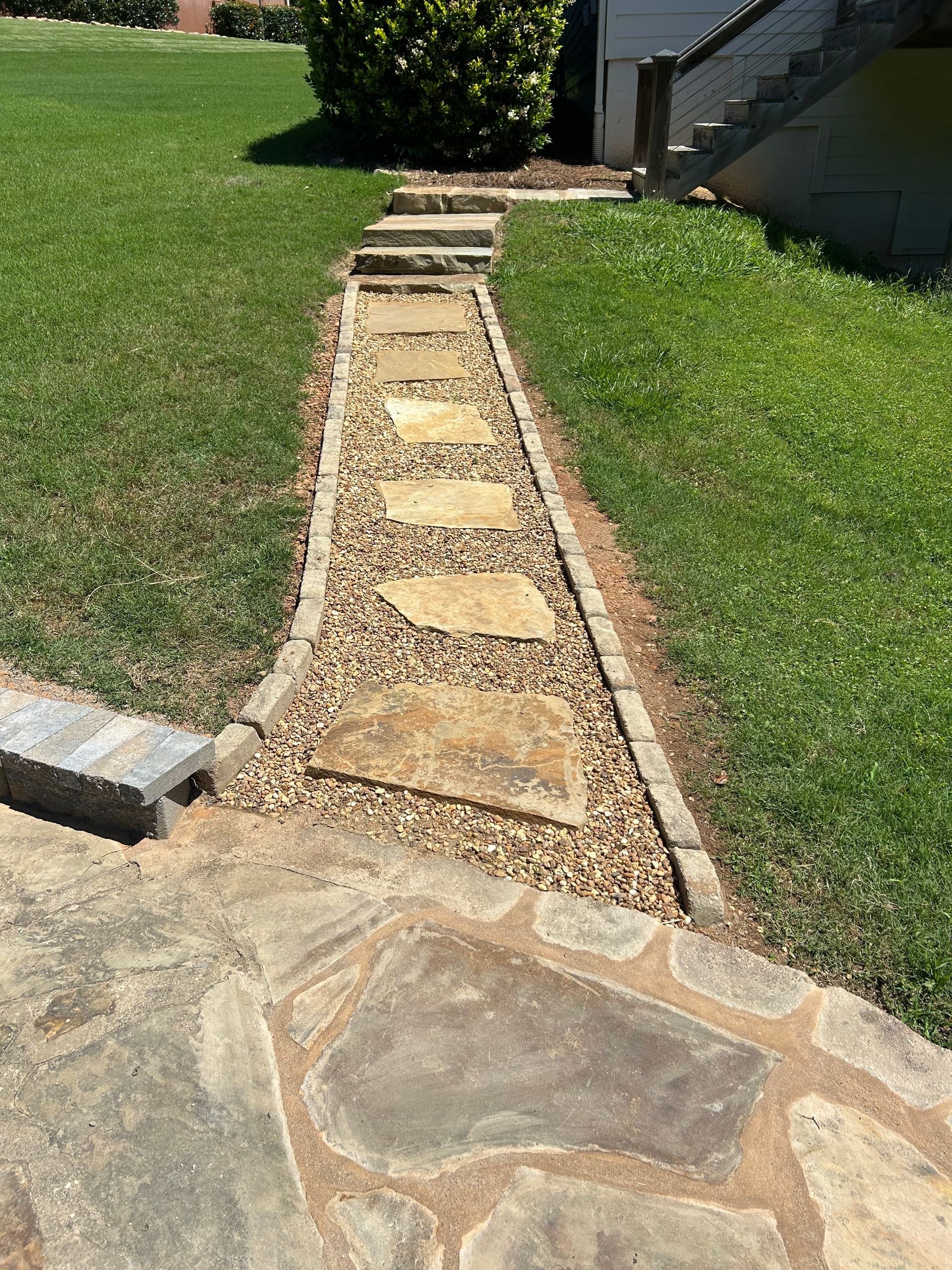 A garden with a stone table and benches, a pergola, and a pathway with greenery and brown mulch.