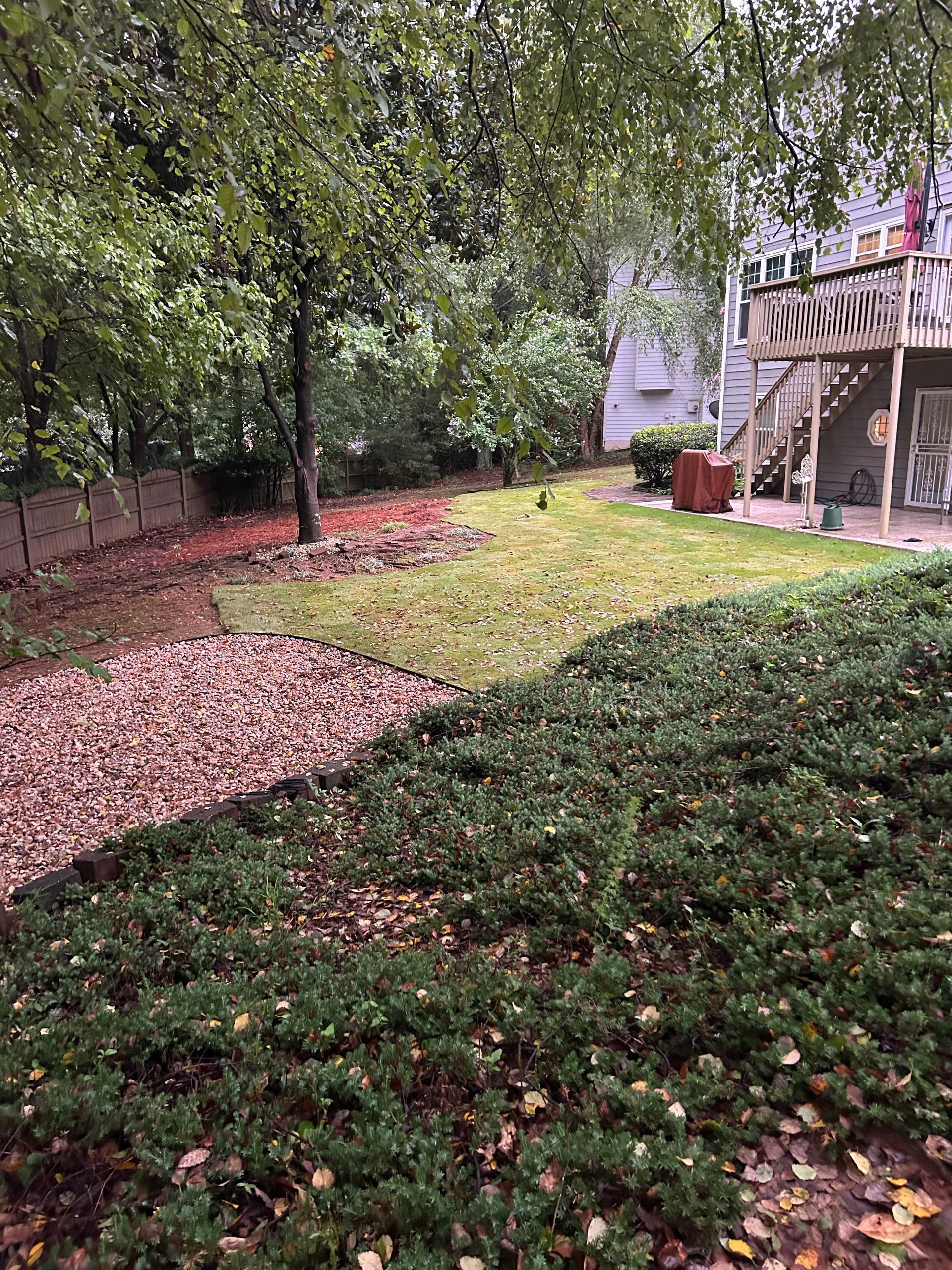 Backyard with green grass, brown mulch, and a wooden deck with a staircase.