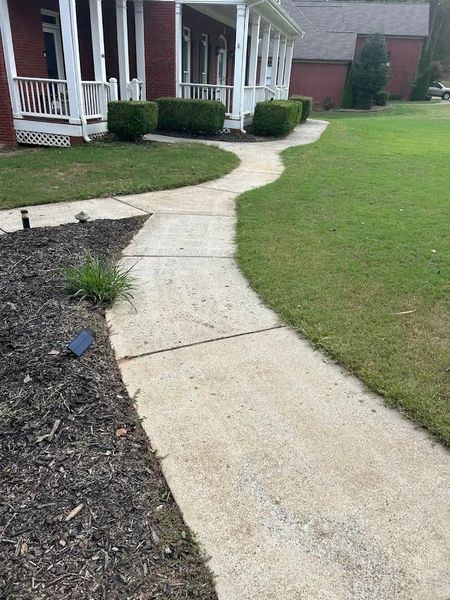 Curving concrete walkway leading to a house with a white porch. Green grass on either side.