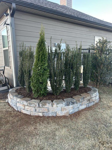 A raised garden bed with stone edging and green shrubs against a beige building.