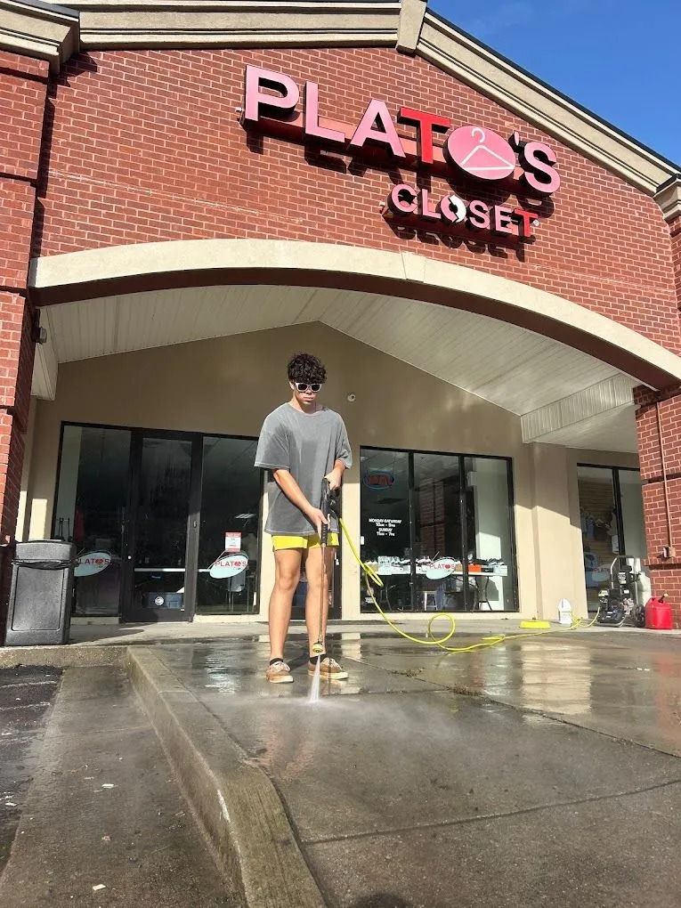 Person pressure washing the sidewalk in front of Plato's Closet store.