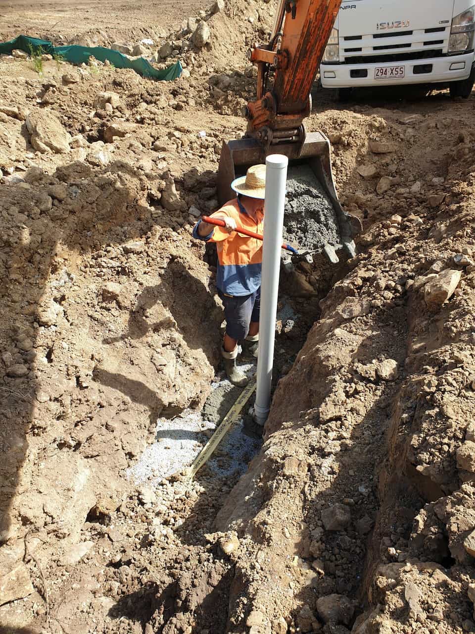 Worker Guiding Concrete From Excavator Bucket Into Trench — Whitsunday Drainage Contractors in Airlie Beach, QLD