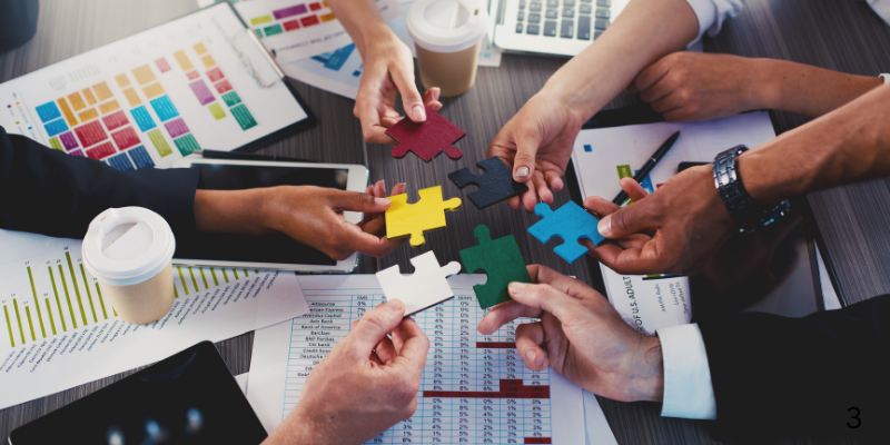A group of people are sitting around a table putting puzzle pieces together.