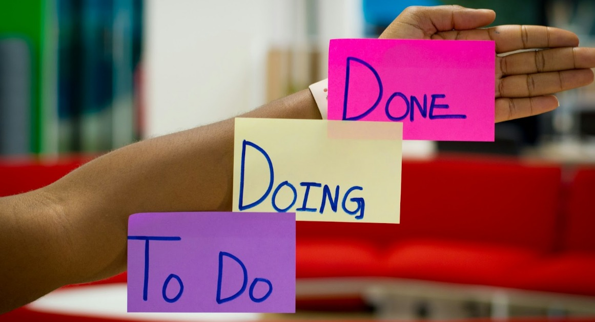 A person is holding three sticky notes that say done doing and to do.