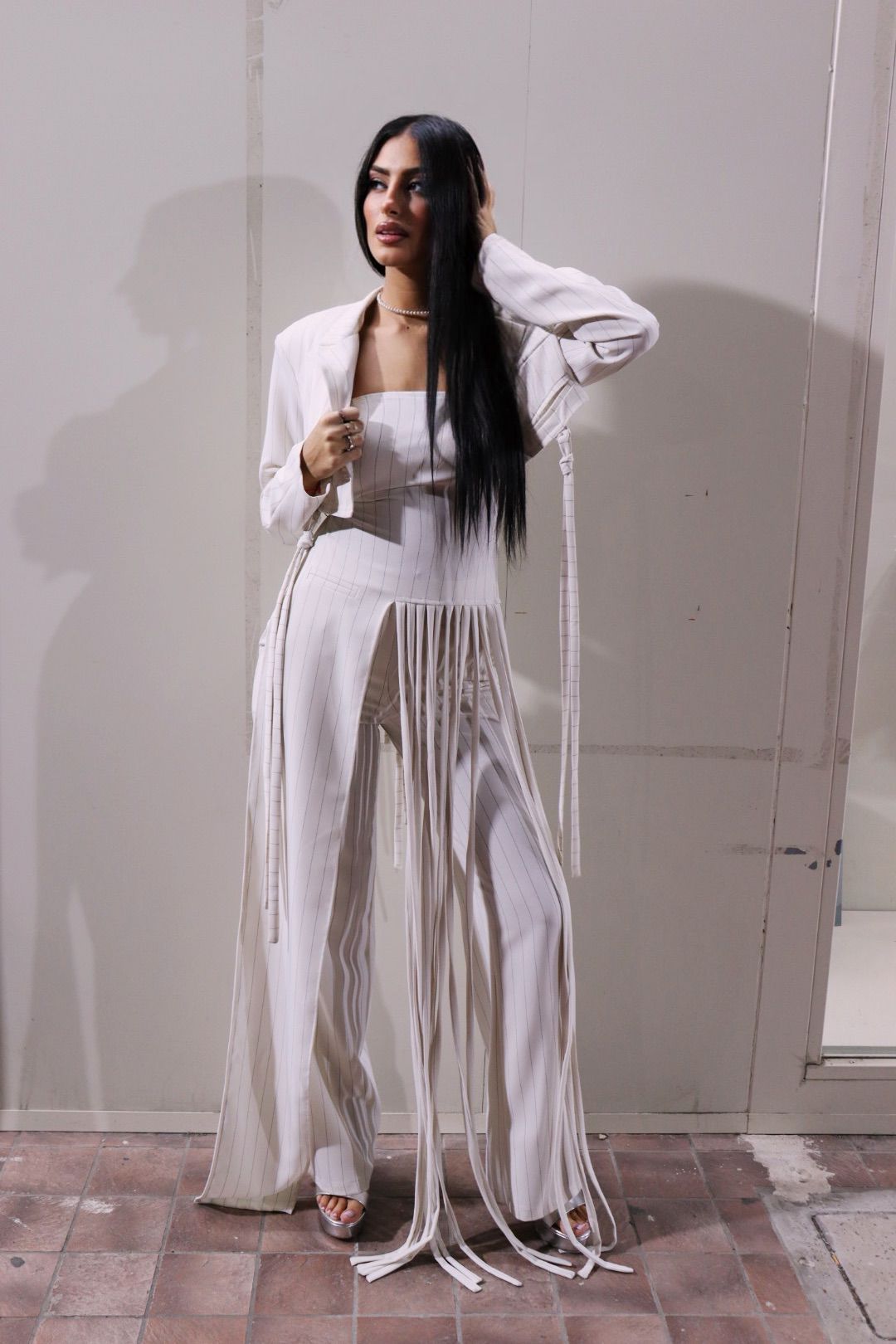 Una donna in un tailleur bianco con le frange è in piedi davanti a un muro.