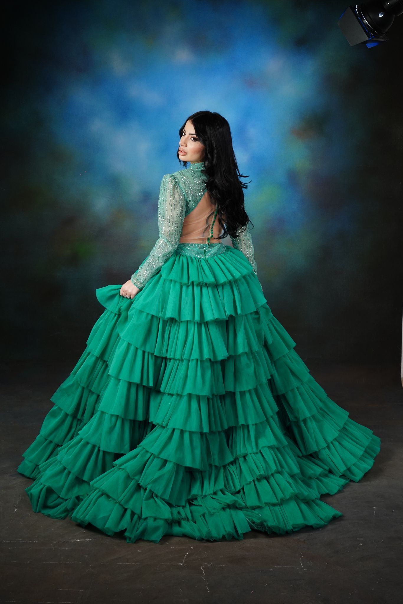 Una donna con un lungo abito verde con volant è in piedi davanti a uno sfondo blu.