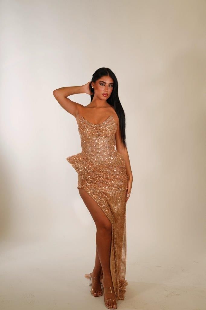 Una donna con un abito dorato è in piedi davanti a un muro bianco.