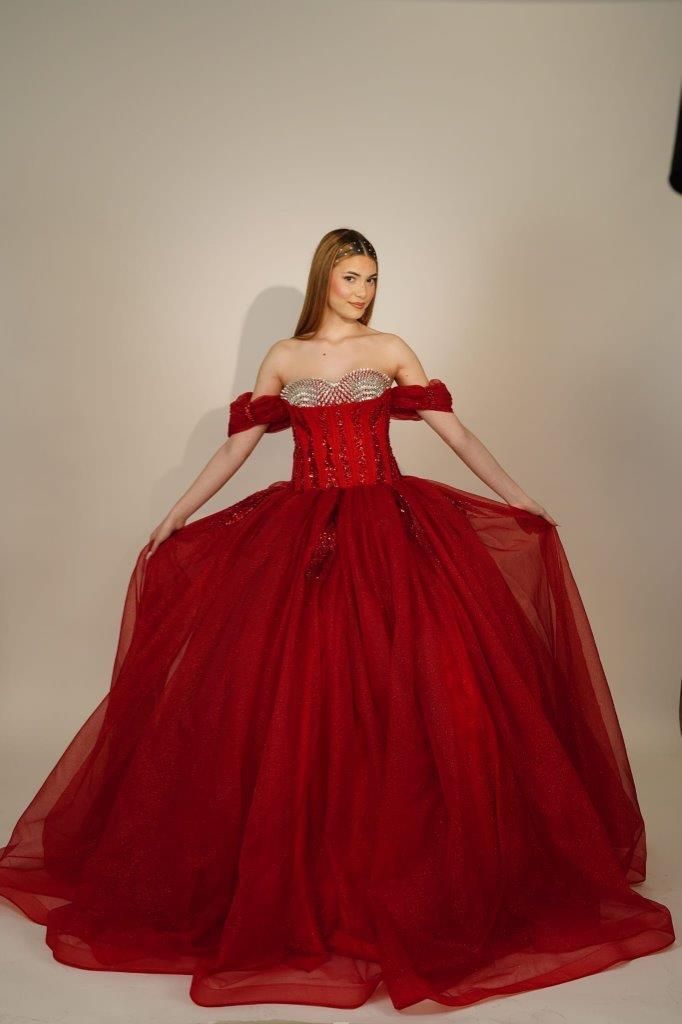 Una donna con un abito da ballo rosso è in piedi davanti a un muro bianco.