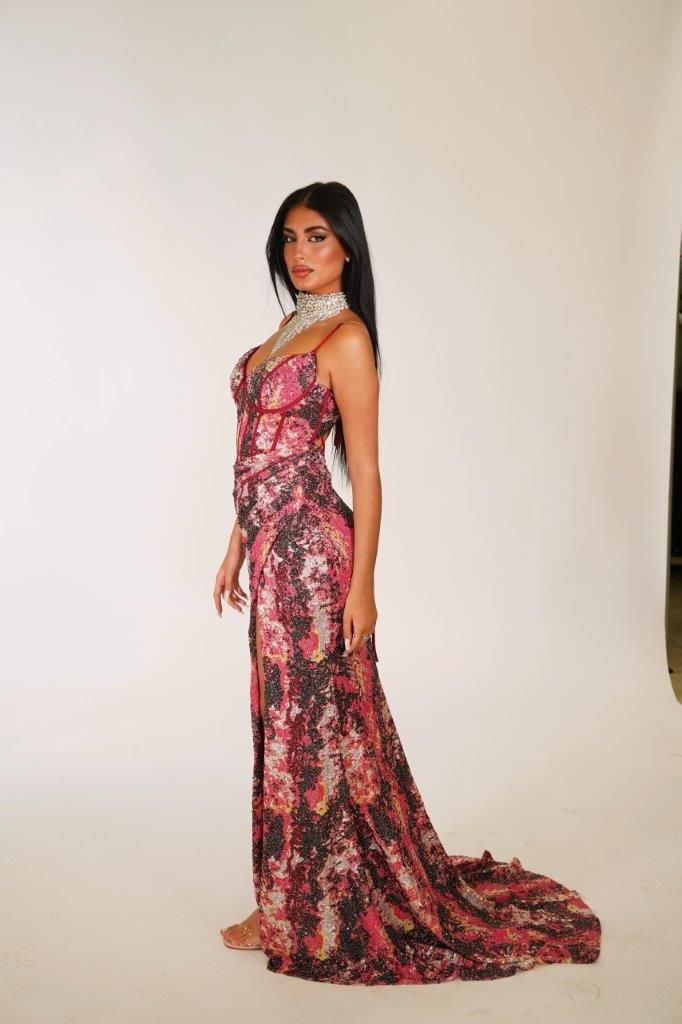 Una donna con un lungo abito rosa è in piedi davanti a un muro bianco.