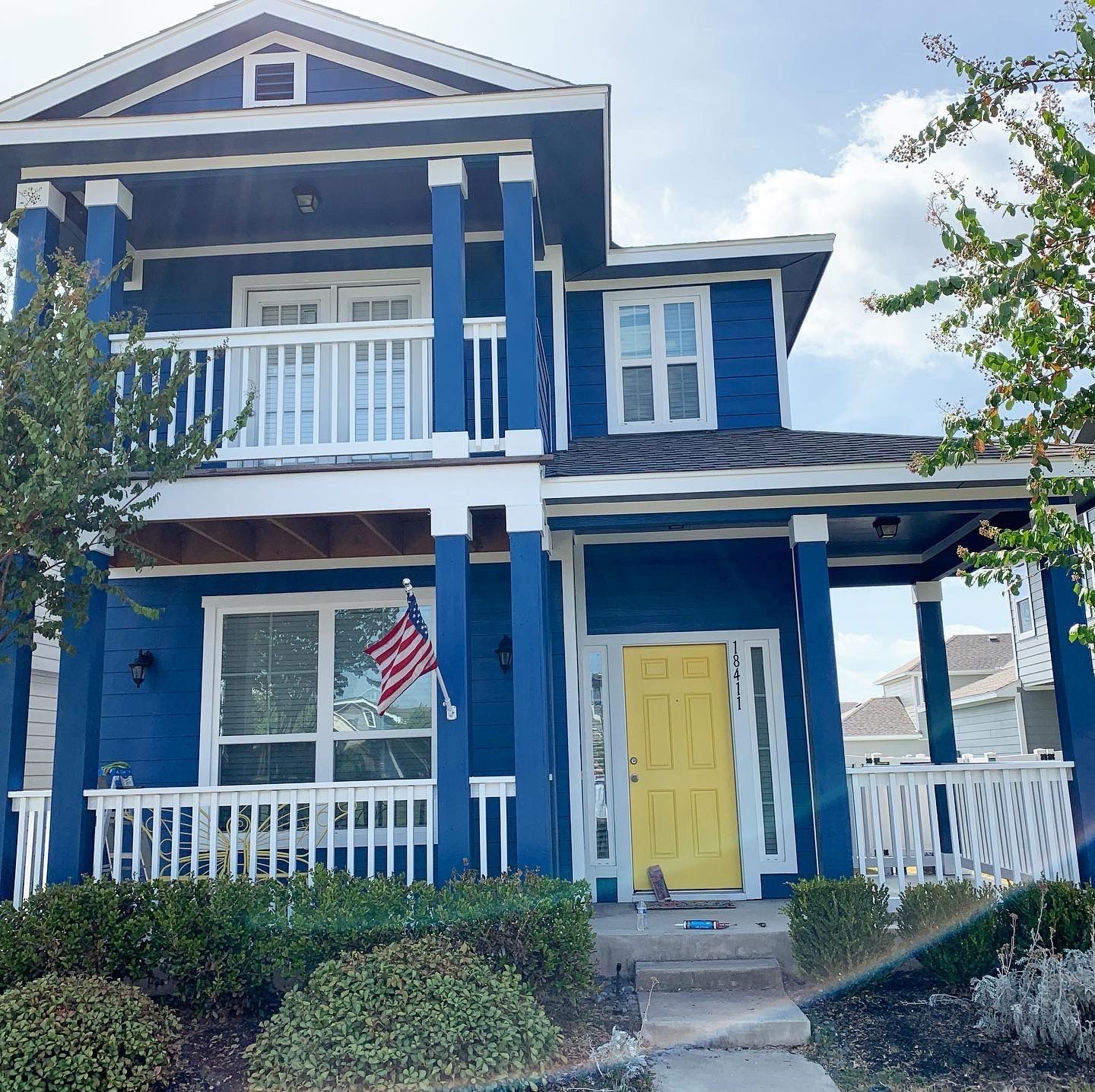 Blue two-story house with white trim, a yellow door, and an American flag.