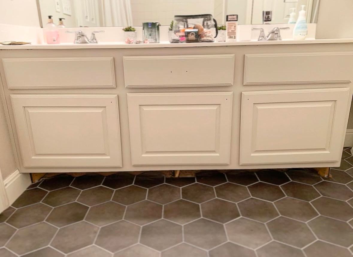 White bathroom vanity with sink and countertop above dark hexagon tile floor
