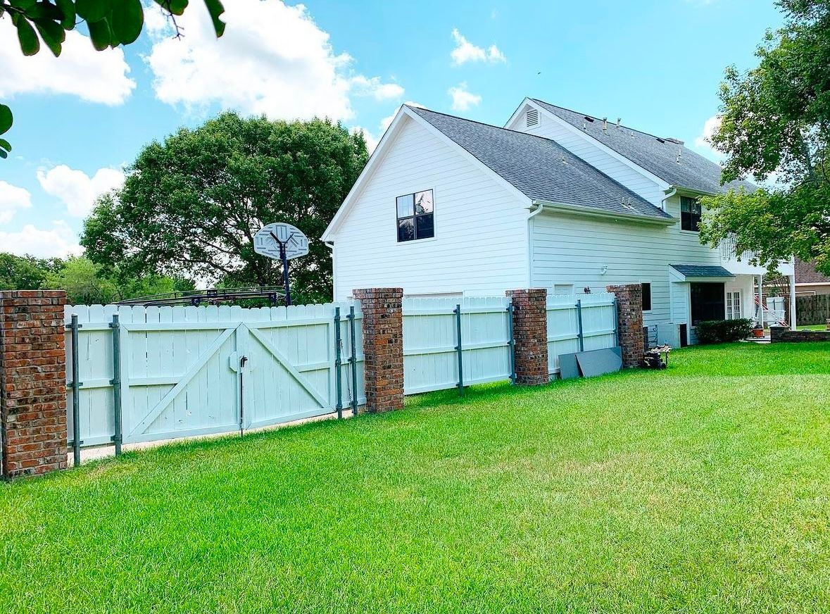 White house behind a fence with brick pillars and a green lawn under a blue sky