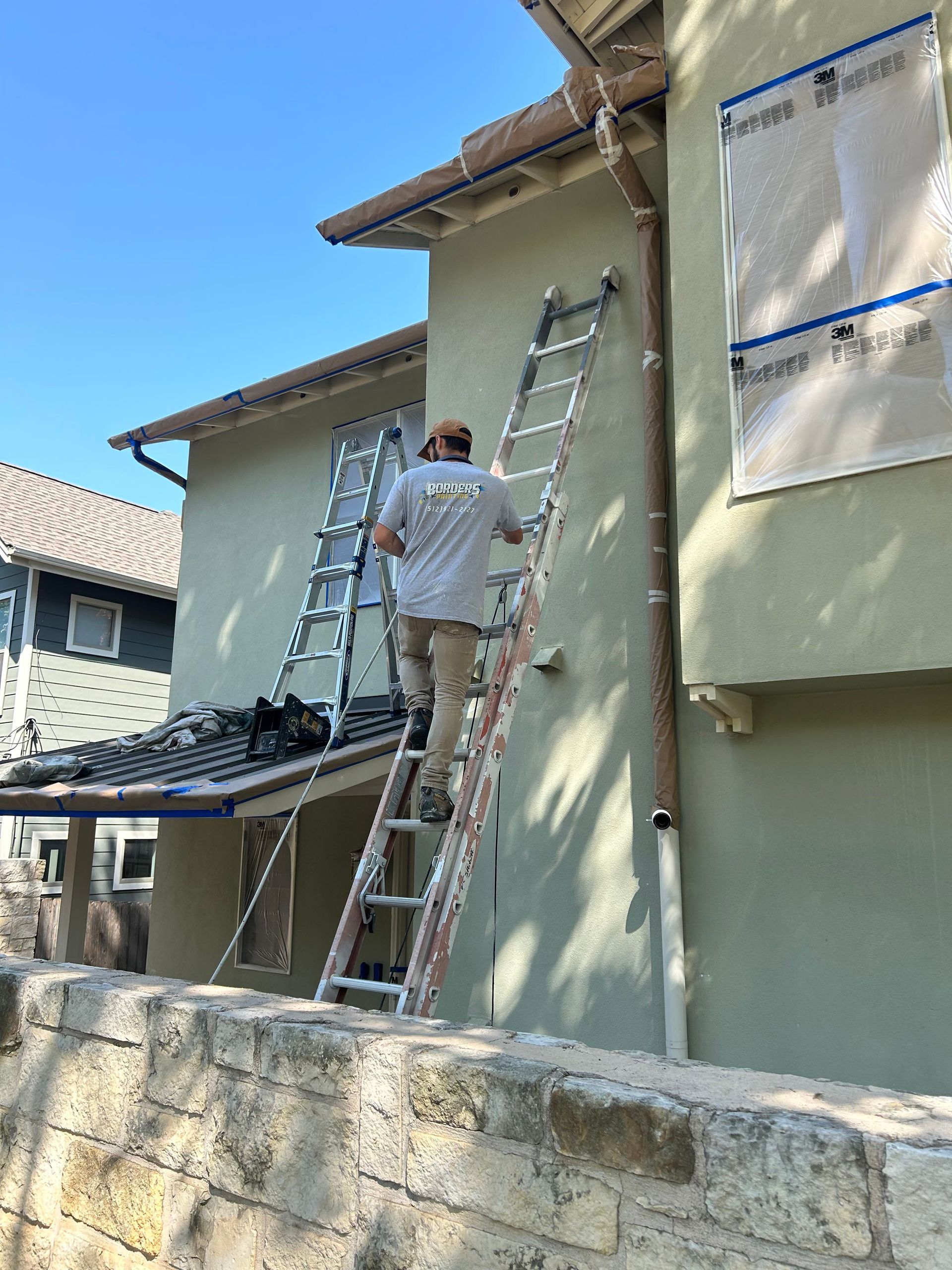 A man is standing on a ladder on the side of a house.