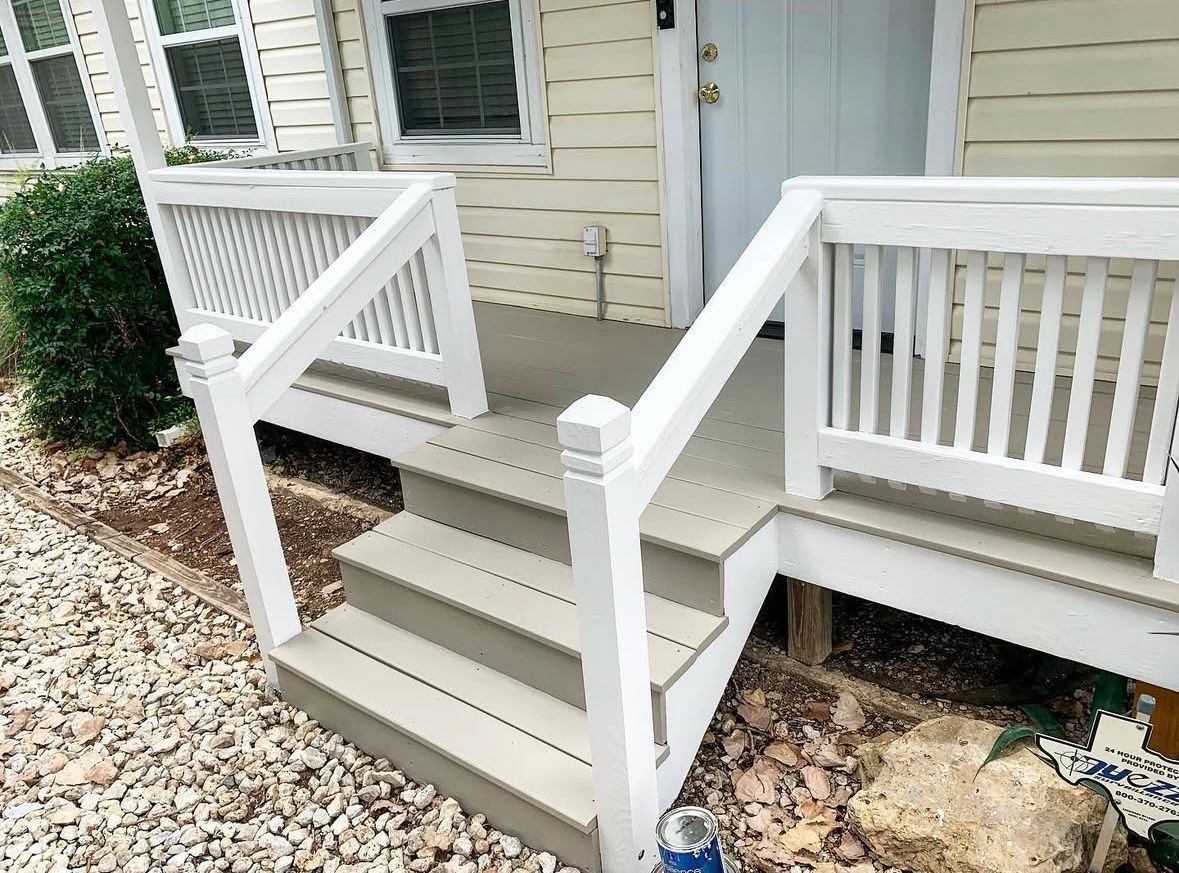 A beige wooden porch with white railings and steps leading to a light-yellow house entrance.