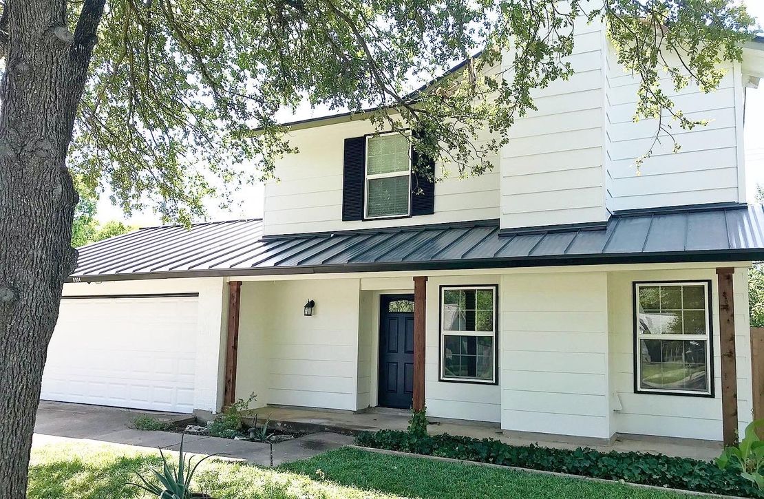 A white house with a metal roof and black shutters.