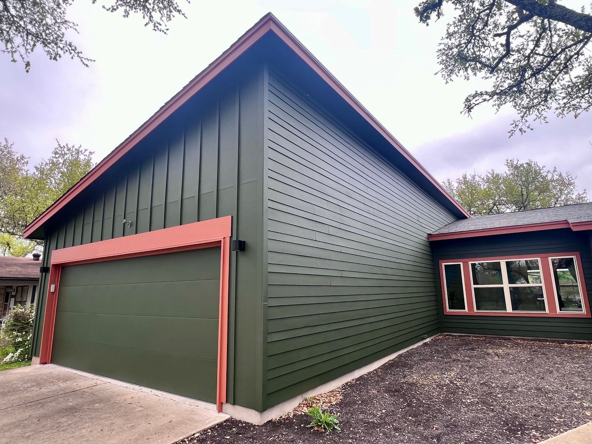 A green house with a red trim and a garage door